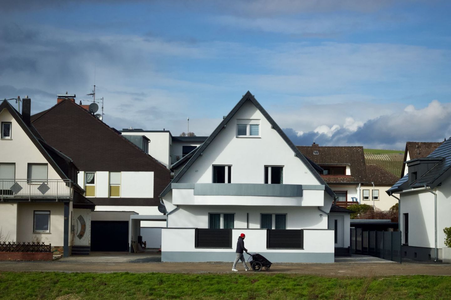Wohnstraße mit frisch verputztem Einfamilienhaus, davor eine unbefestigte Zufahrt und eine Wiese